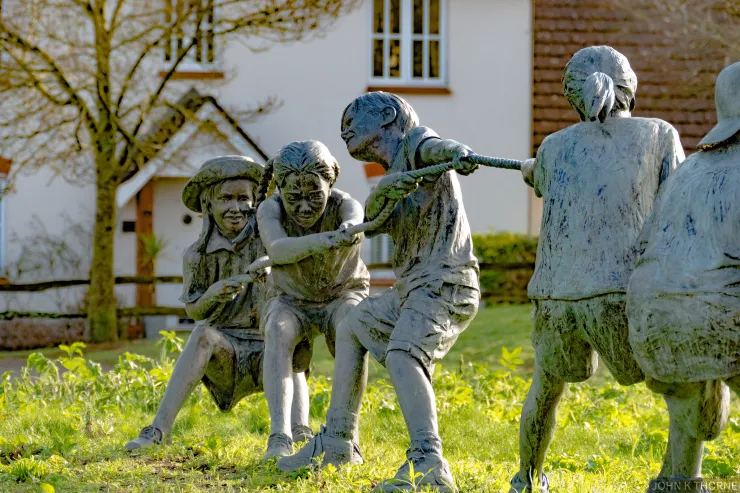 Statue of three boys, three girls and a dog playing tug of war by W Stanley Proctor